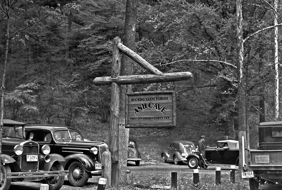A wooden Ash Cave entrance sign beside parked cars in 1937.