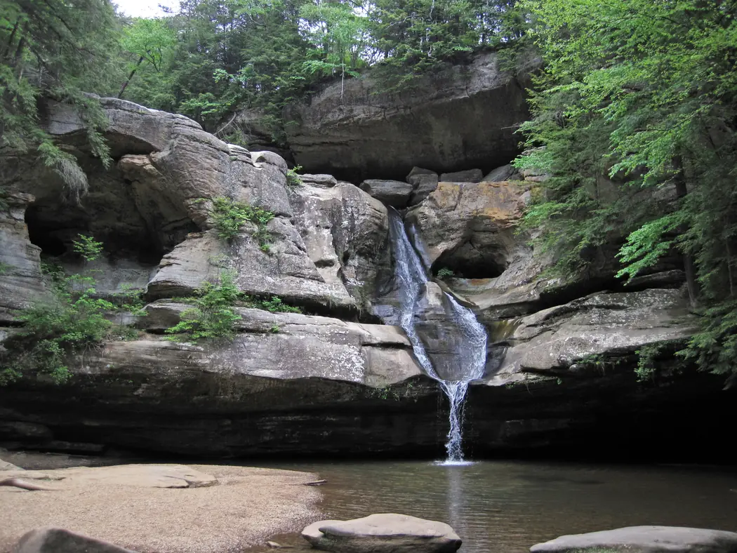 Cedar Falls cascading down sandstone surrounded by green trees in Hocking Hills